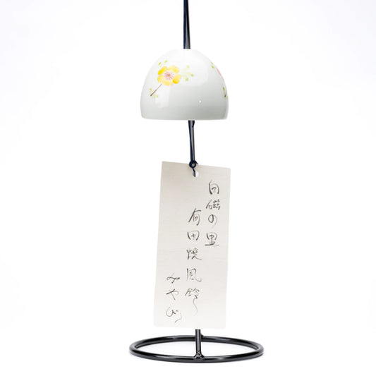 Floral porcelain wind chime and paper strip hanging from a black display stand on white.
