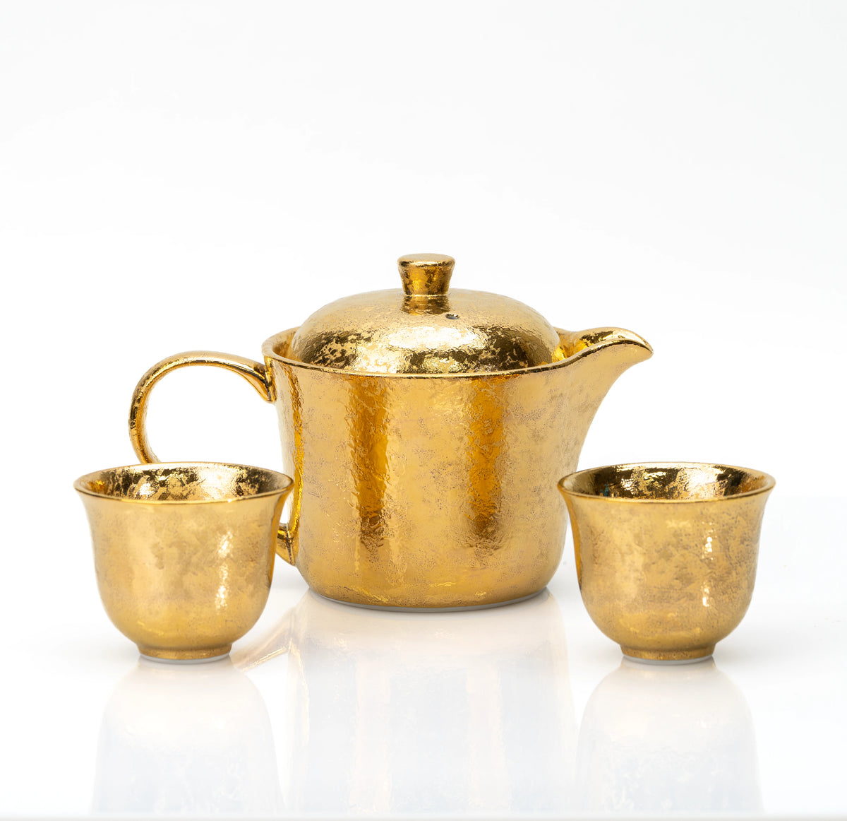 Gold-glazed porcelain teapot and two matching cups on white.