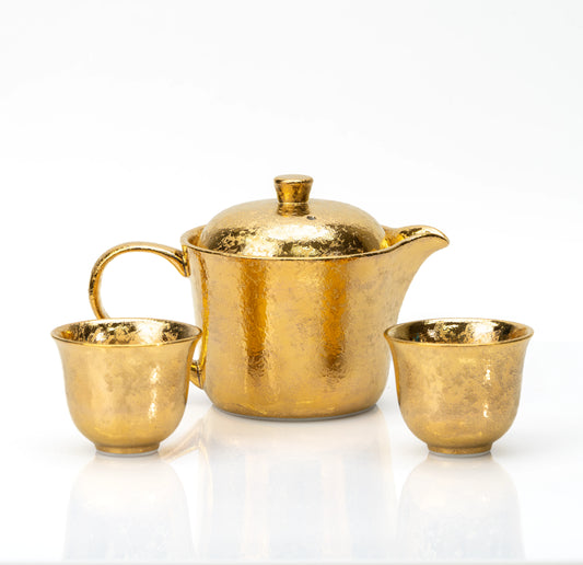 Gold-glazed porcelain teapot and two matching cups on white.