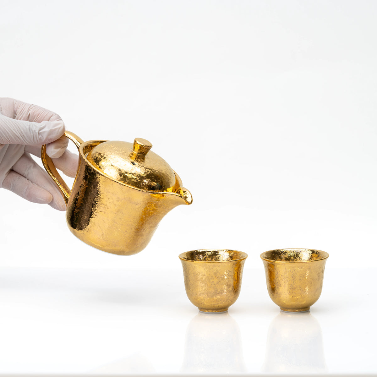 Gold teapot held above the two matching cups.