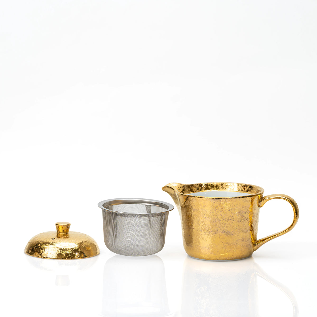 Gold teapot with its lid removed beside a metal mesh strainer.