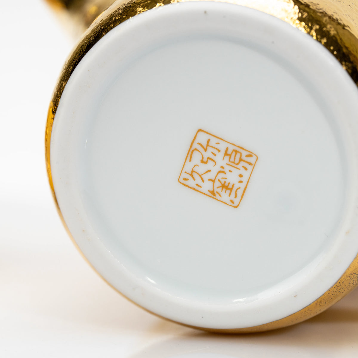 White underside of the gold teapot with a gold maker's mark.