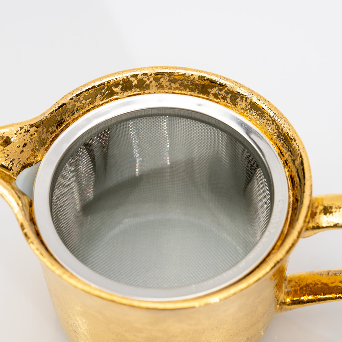 Top view into the gold teapot and its mesh strainer.