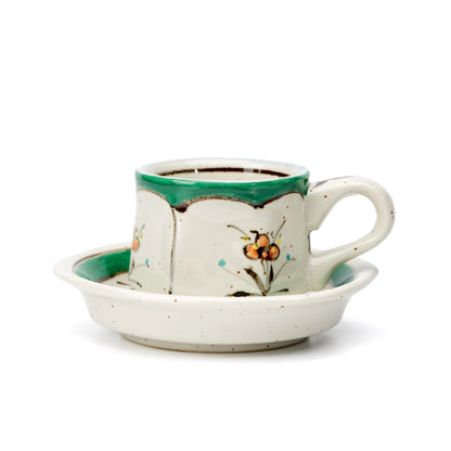 Green-rimmed hexagonal porcelain demitasse cup and saucer with small flowers on white.