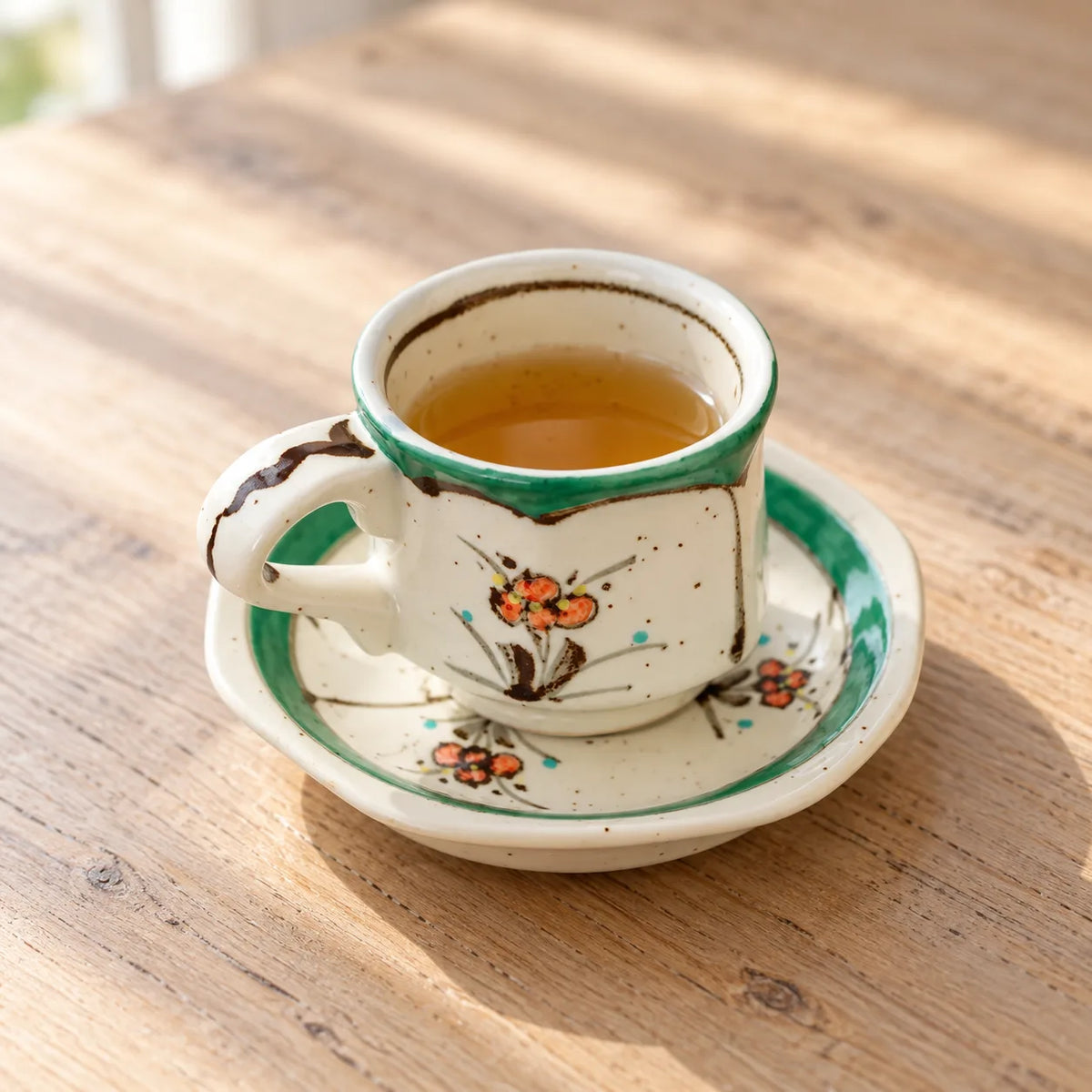 Small Arita green floral demitasse cup holding amber tea on its matching saucer in soft window light.