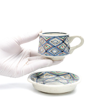 Demitasse cup held above its matching saucer in a gloved hand.