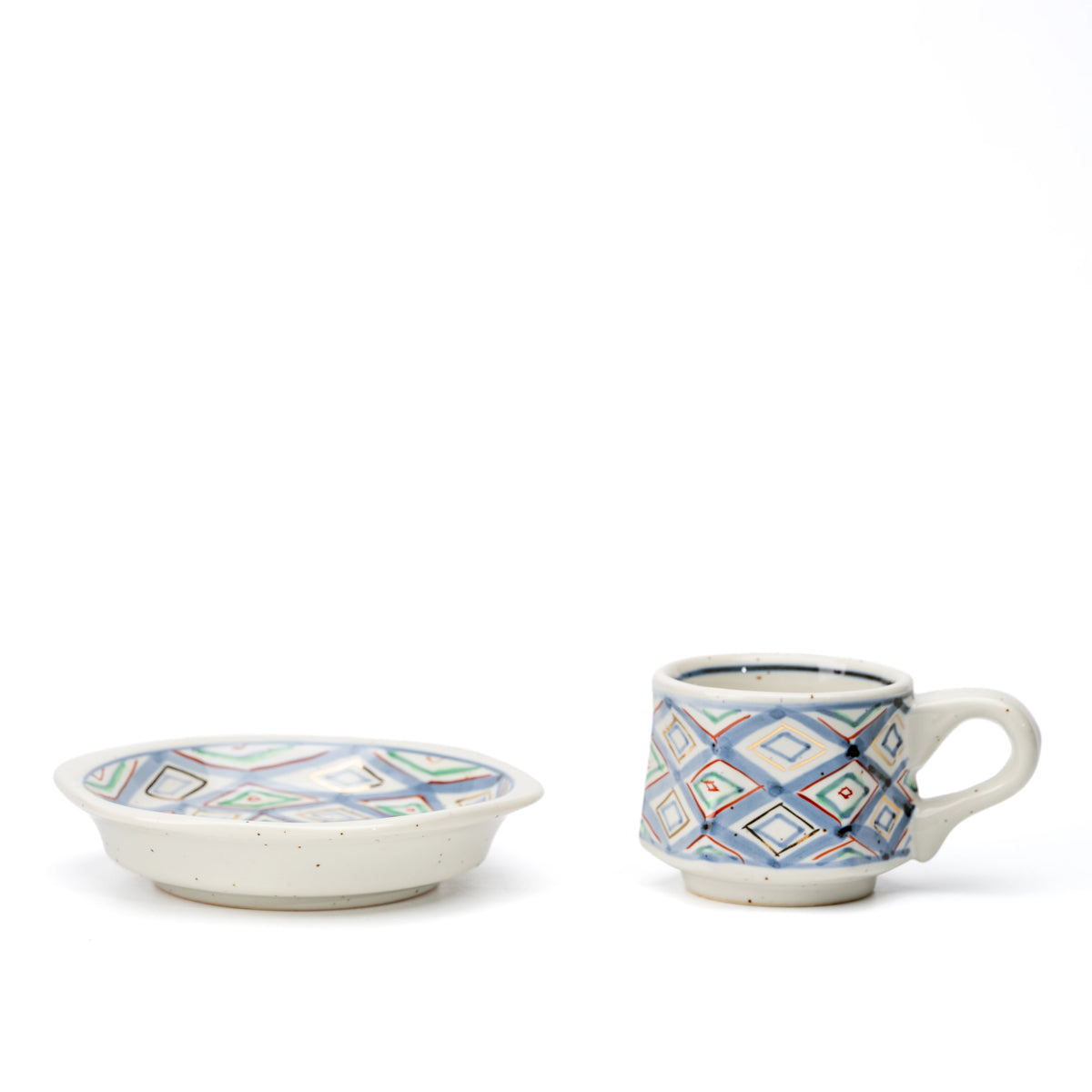 Diamond-pattern cup and saucer placed separately on white.