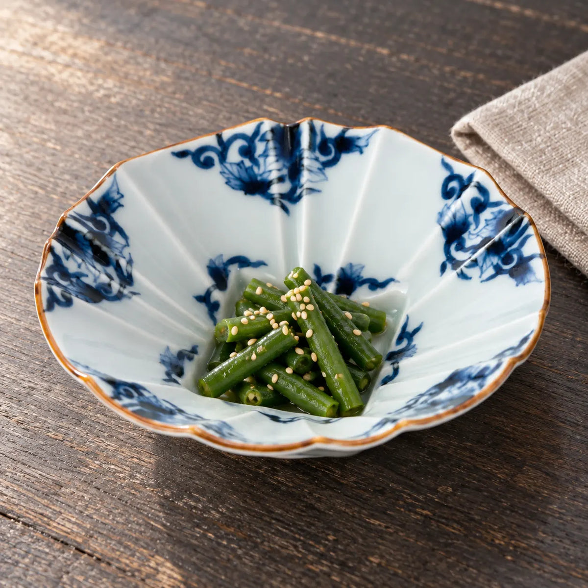 A shallow blue-and-white karakusa bowl with faceted sides, holding a small serving of sesame-dressed green beans