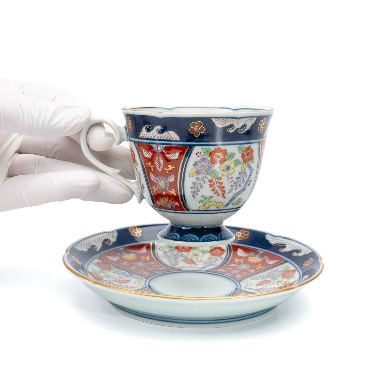 Floral porcelain cup held above its matching saucer in a gloved hand.