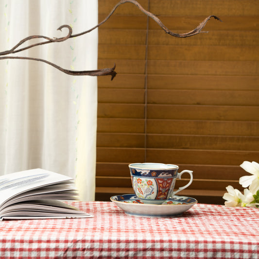 Blue and red floral cup and saucer on a red checked tablecloth beside a book.