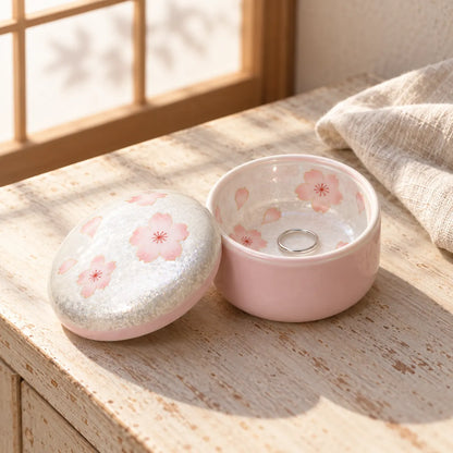 Open Arita pink cherry blossom lidded box holding a small silver ring beside its domed lid