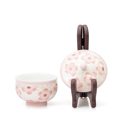Open pink teacup with its lid displayed upright on a small stand.