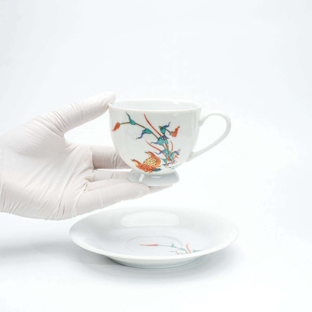 Porcelain cup with quail and red berries held in a gloved hand.
