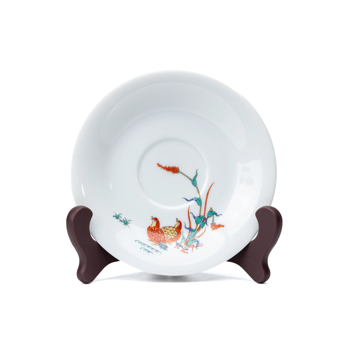 White porcelain saucer with quail and red berries, viewed from above.
