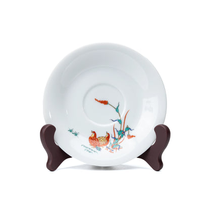 White porcelain saucer with quail and red berries, viewed from above.