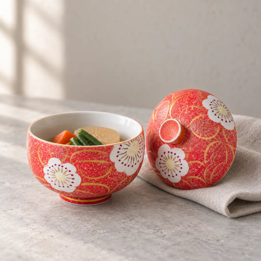 A red Arita floral lidded bowl holding a small serving of simmered vegetables, with its matching lid beside it