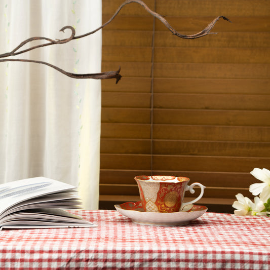Red and gold cup and saucer on a red checked tablecloth beside a book.