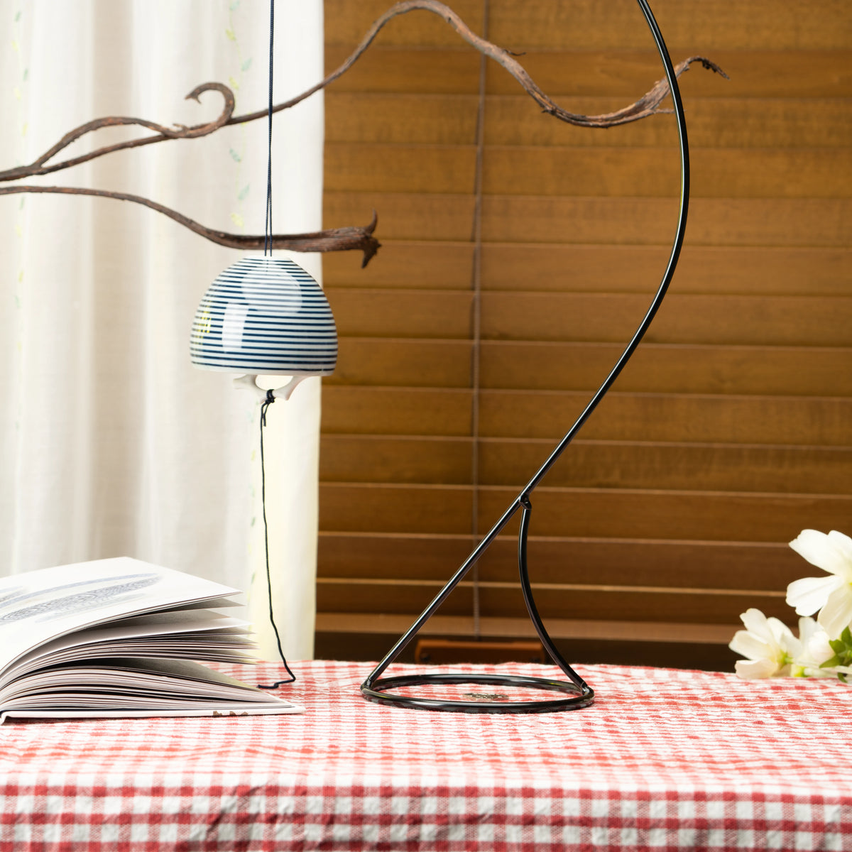 Striped porcelain wind chime hanging from a display stand on a red checked tablecloth.