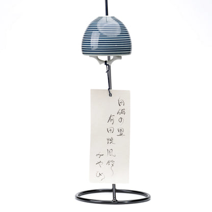 Striped porcelain wind chime and paper strip hanging from a black display stand on white.