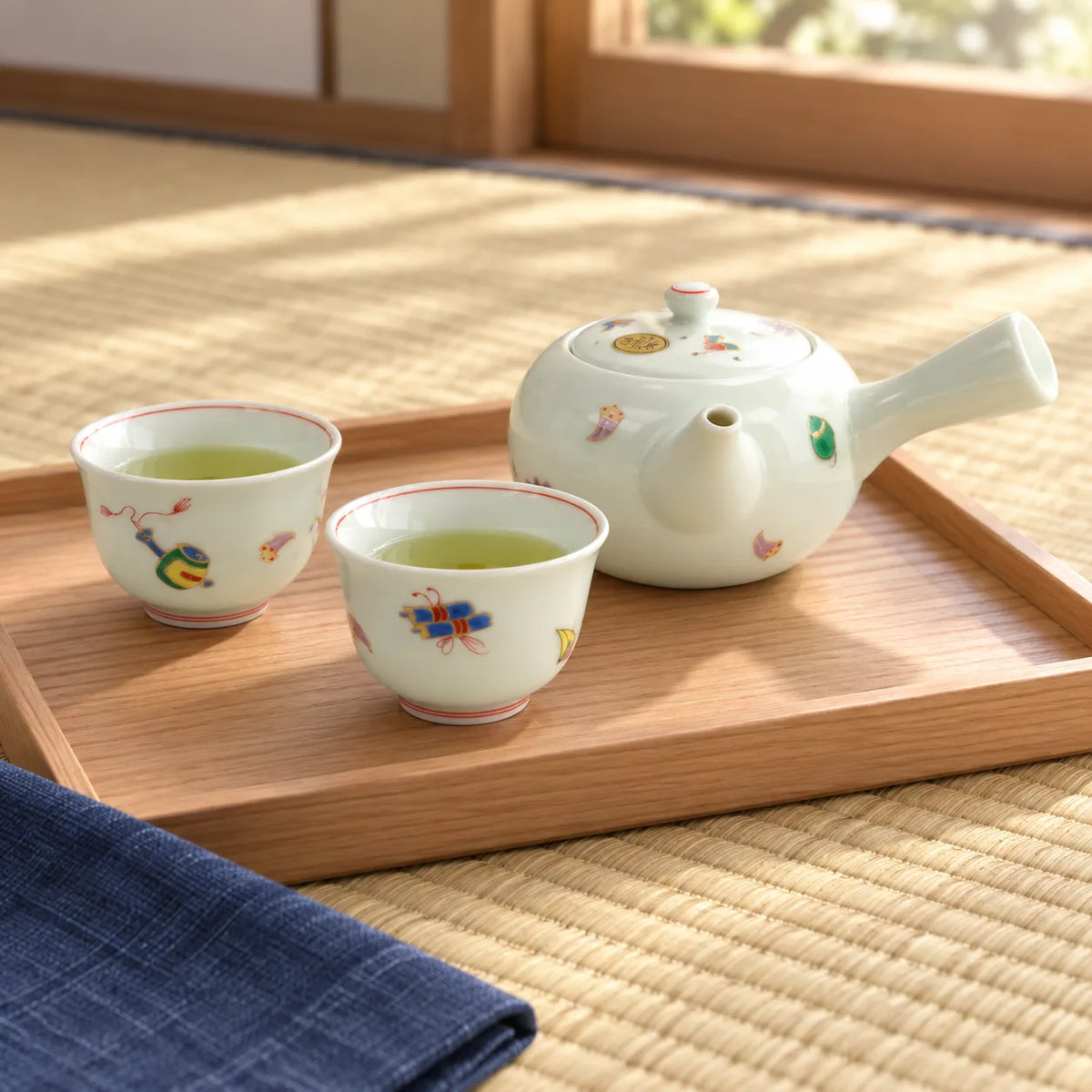 Arita Takarazukushi side-handle teapot with two matching cups on a cedar tray