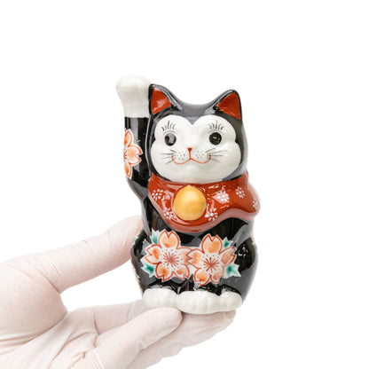Black Kutani lucky cat held in a gloved hand, showing its size and cherry blossom decoration.