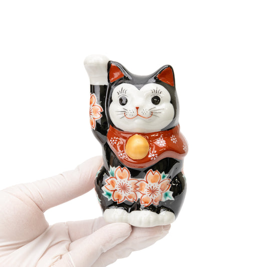 Black Kutani lucky cat held in a gloved hand, showing its size and cherry blossom decoration.