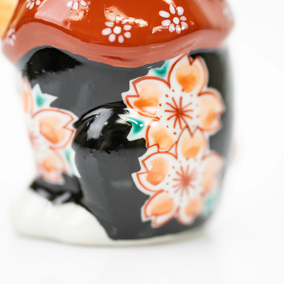 Close-up of cherry blossoms on the lucky cat's glossy black body below the red bib.