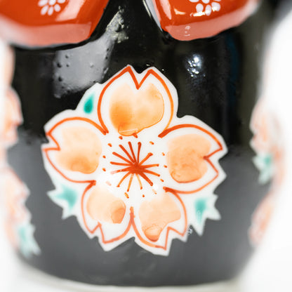 Close-up of a peach-colored cherry blossom against the lucky cat's black glaze.