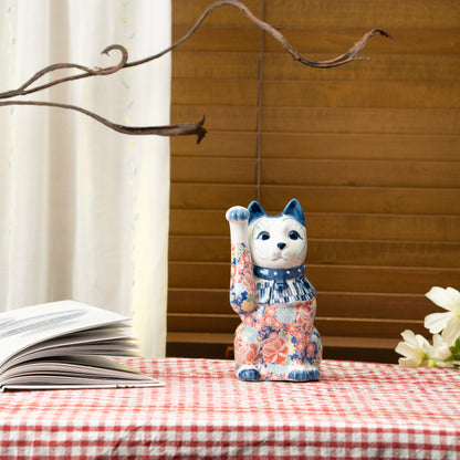 Blue floral lucky cat on a red checked tablecloth beside a book.