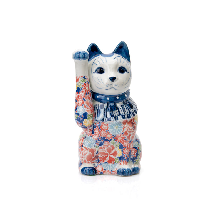 Blue and white porcelain lucky cat with a raised paw and dense pink floral decoration on white.