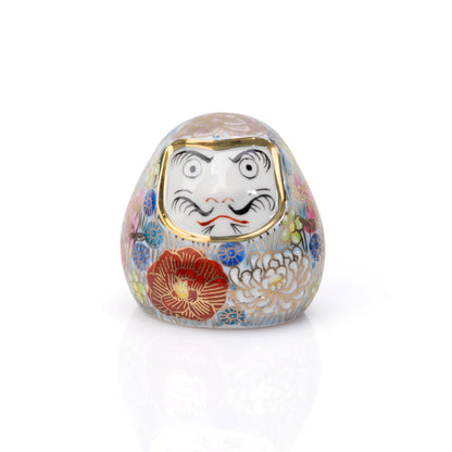 Small Kutani daruma covered in multicolored flowers with a white face on white.