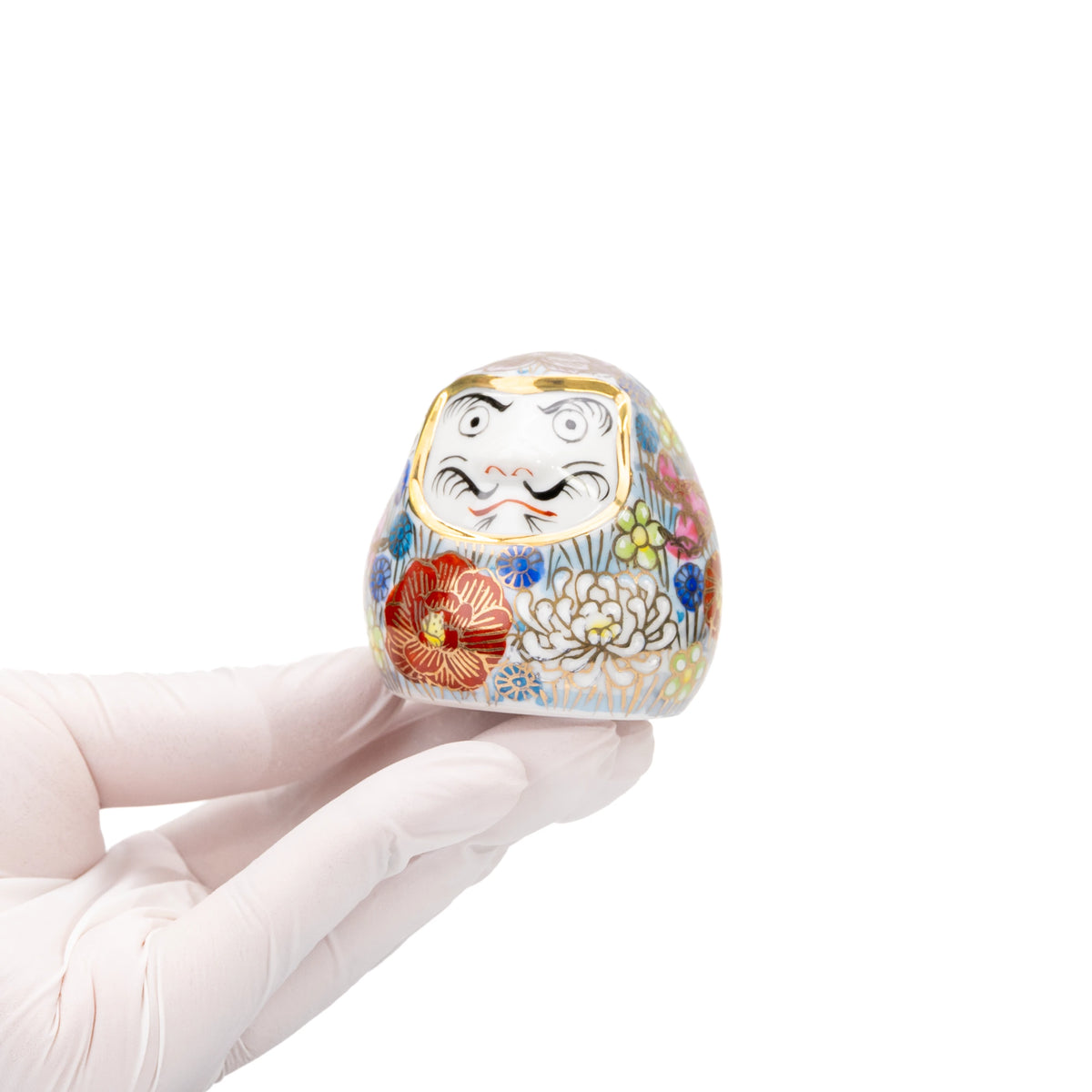 Small floral Kutani daruma held in a gloved hand.