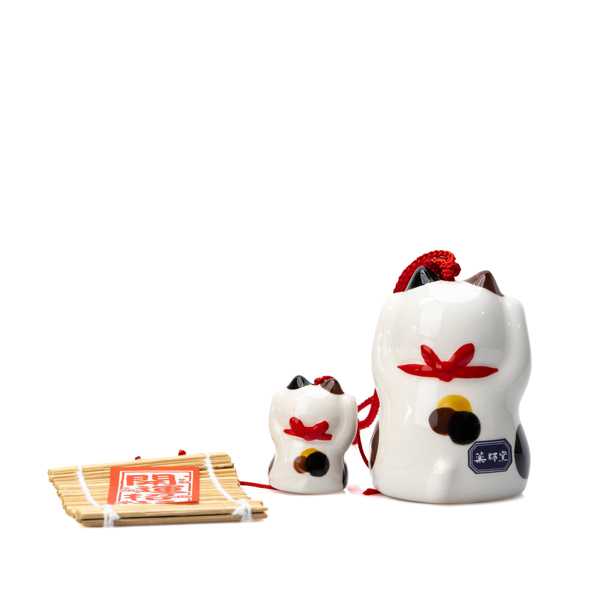 Backs of the calico cat and kitten wind chime beside the paper strip.