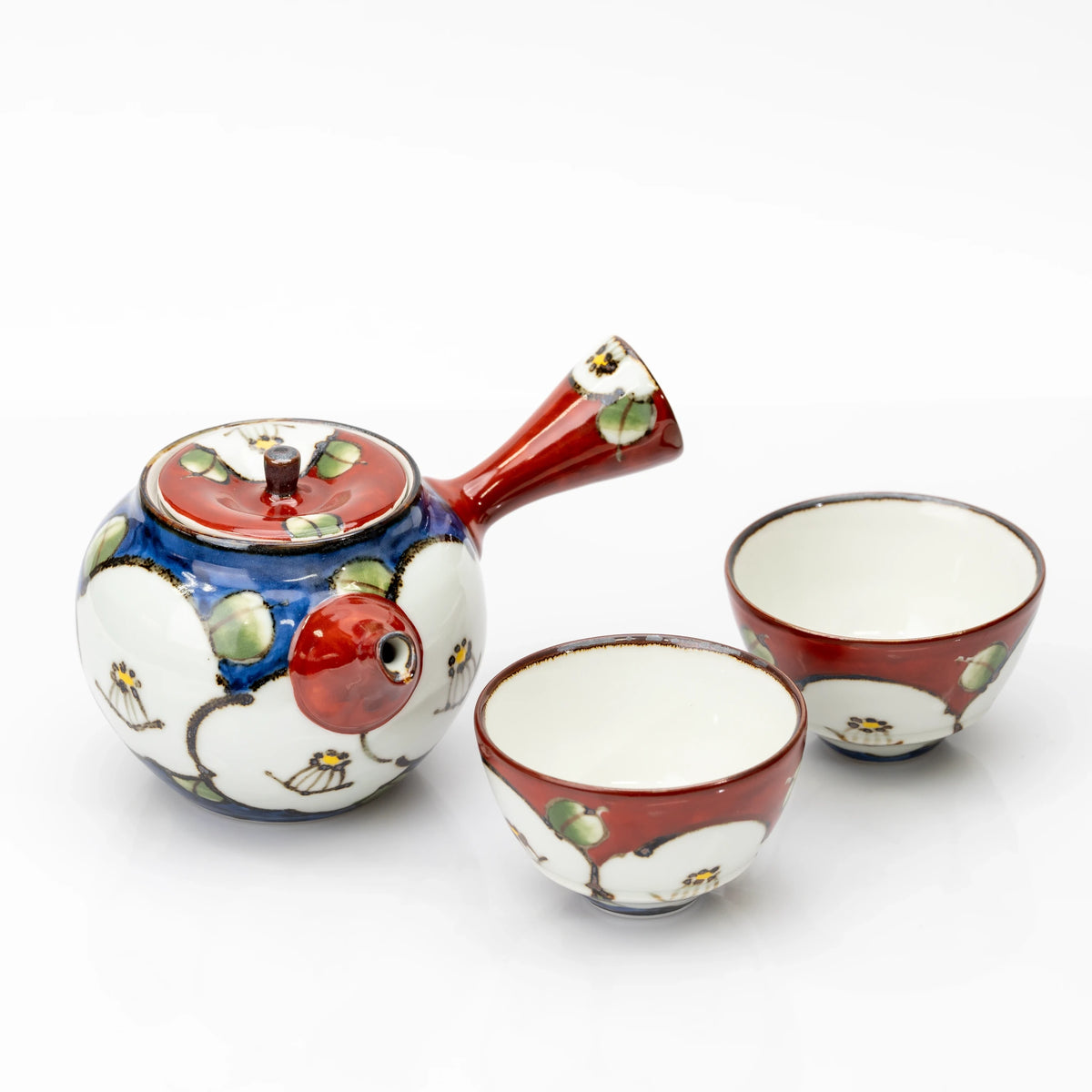 Japanese tea set with a blue camellia teapot, red side handle and lid, and two red cups with white interiors.