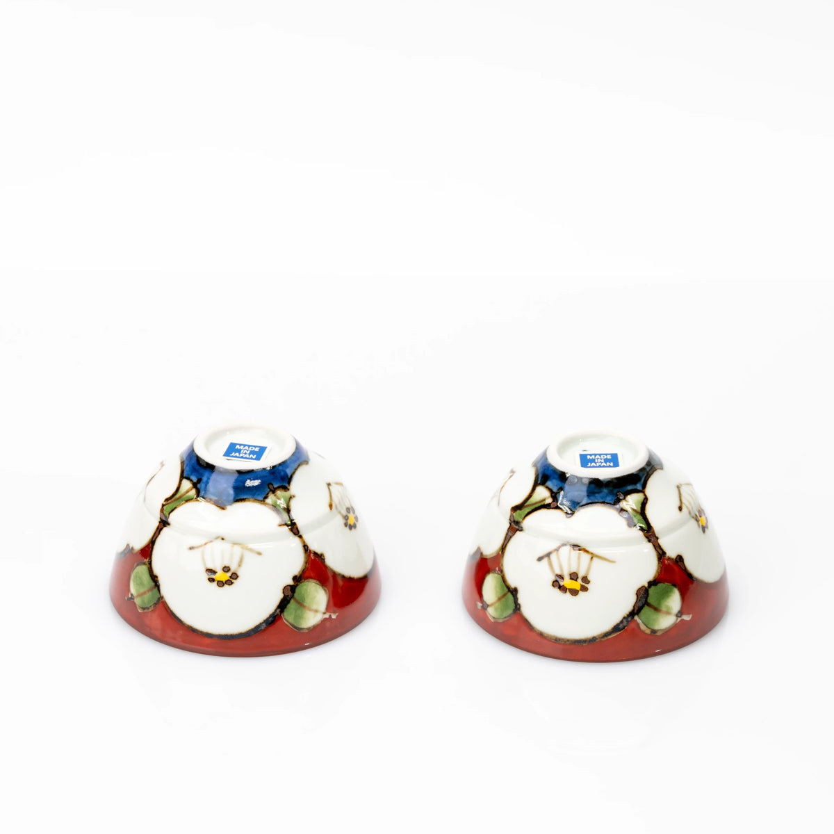 Two matching red camellia cups turned upside down, showing blue decoration around the bases and Made in Japan stickers.