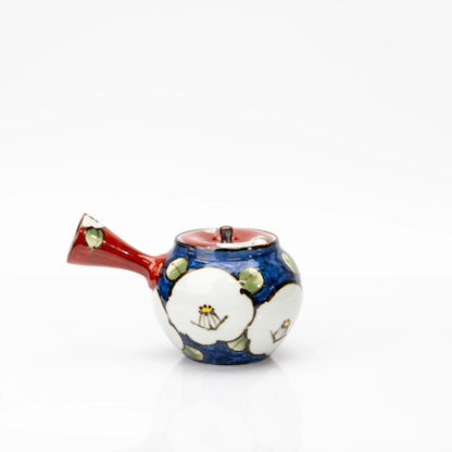 Rear view of the blue camellia teapot with white flowers, green leaves, a red lid and a flared red side handle.