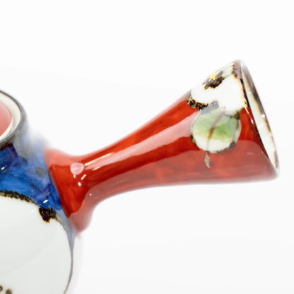 Close-up of the flared red side handle with white camellia petals, a green leaf and dark edging.