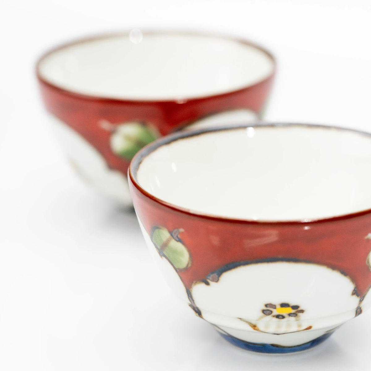 Close-up of two red camellia cups, showing their white interiors, dark-edged rims and green leaf decoration.