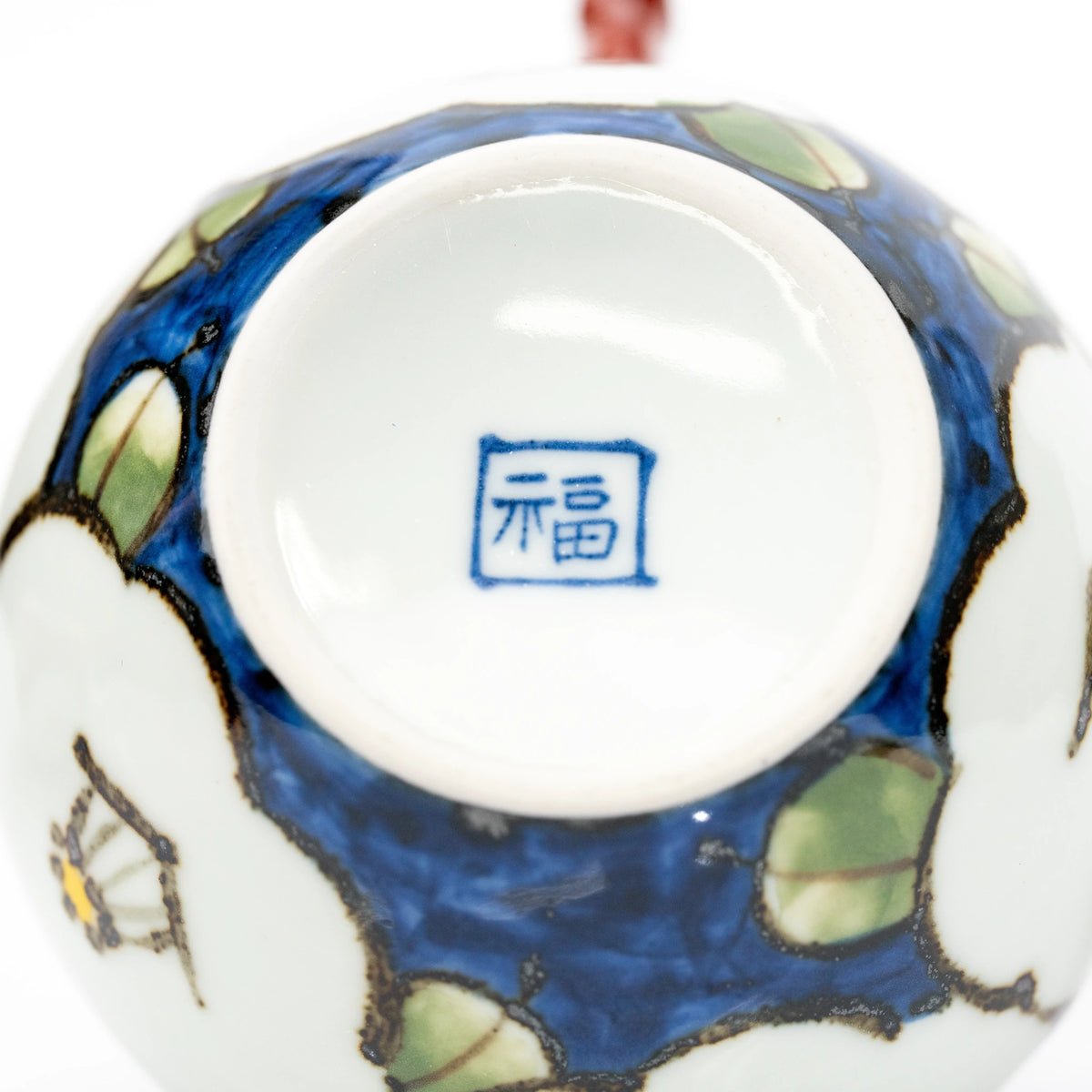 Close-up of the teapot’s white base with a blue square 福 mark, surrounded by blue glaze and green leaves.