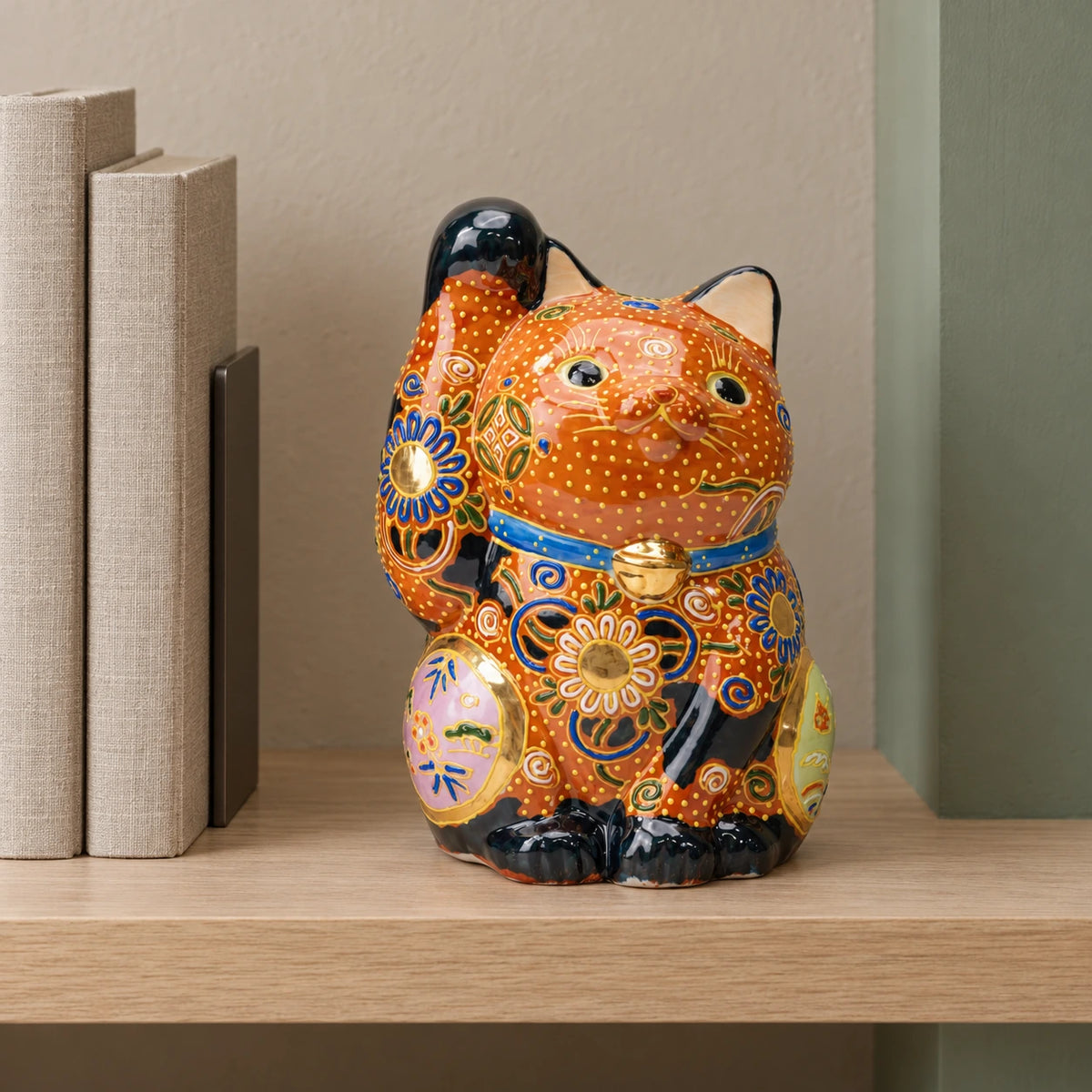 Copper-orange Cha-Mori lucky cat with raised floral decoration on an oak shelf beside two neutral-colored books.