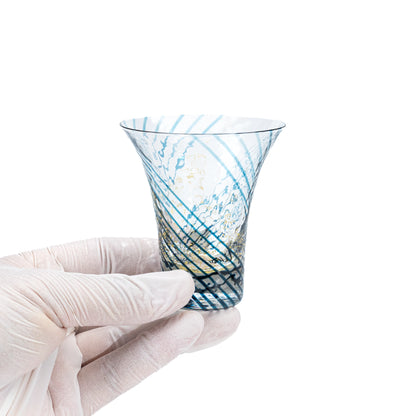 Blue and gold-colored glass sake cup held in a gloved hand.