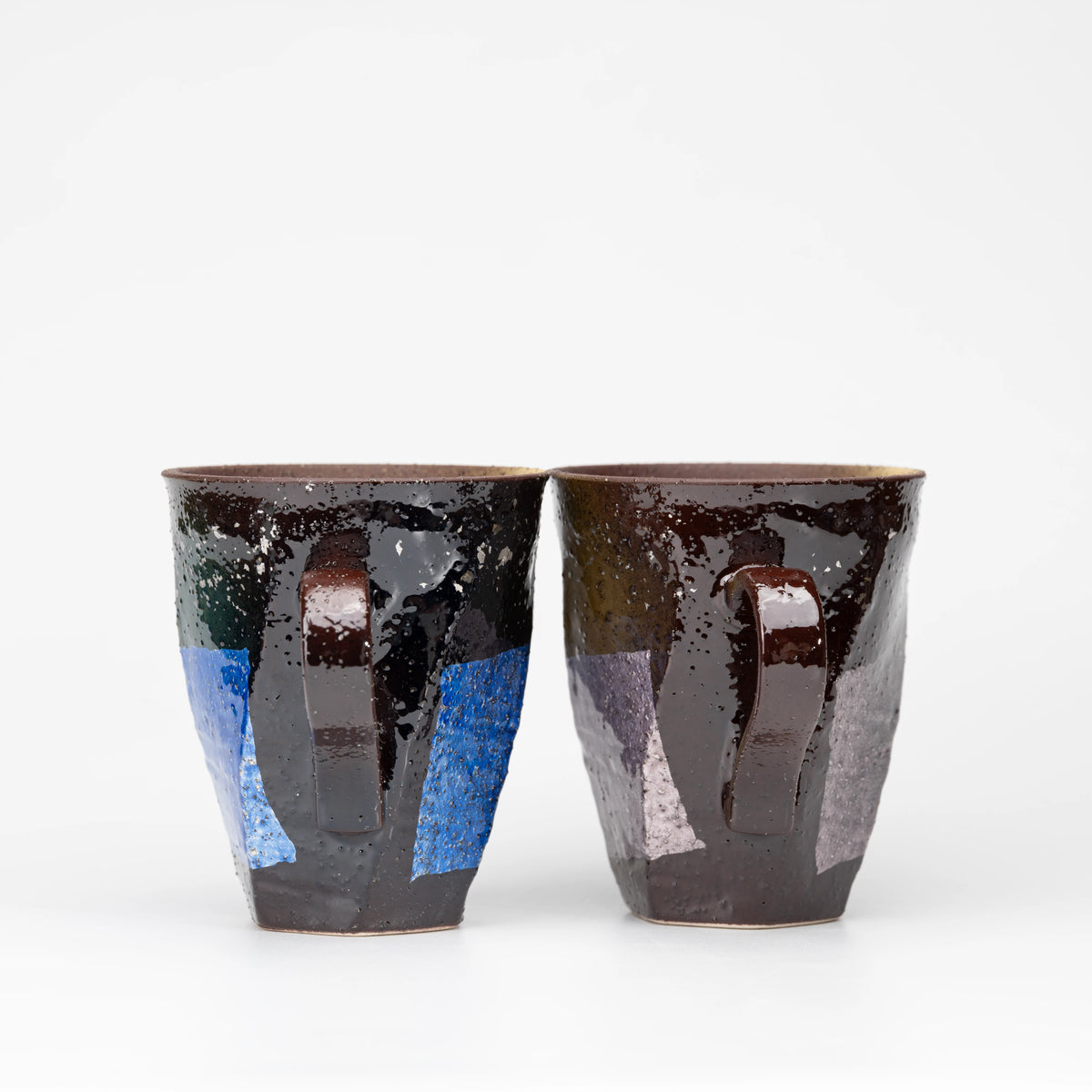 Rear view of the two faceted mugs and their dark loop handles.