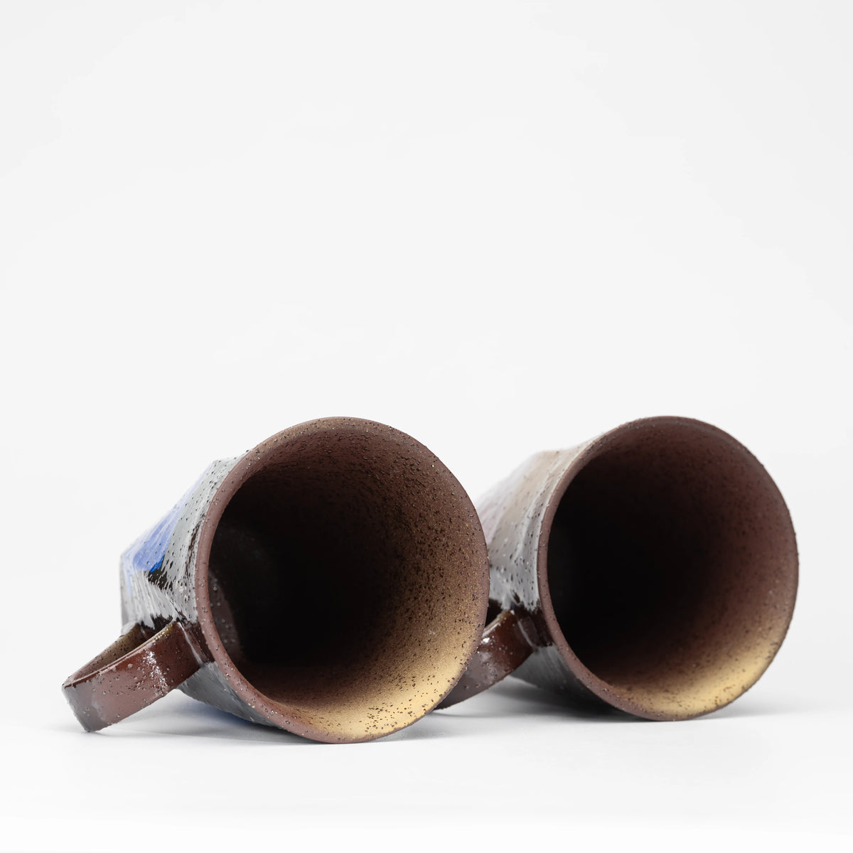 Top view into the warm brown interiors of the mug pair.