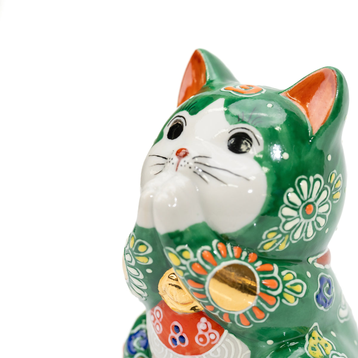 Close-up of the green cat's white face, joined paws and gold bell.