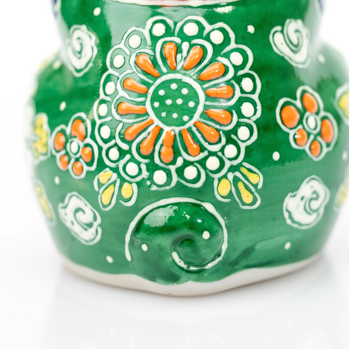 Raised floral decoration and curled tail on the cat's green back.