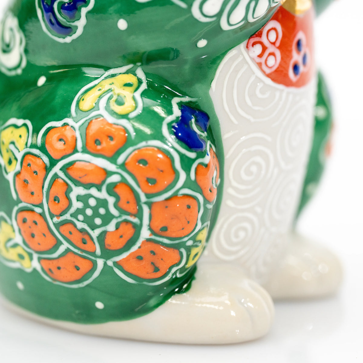 Orange flower and white scroll decoration on the green cat's side.