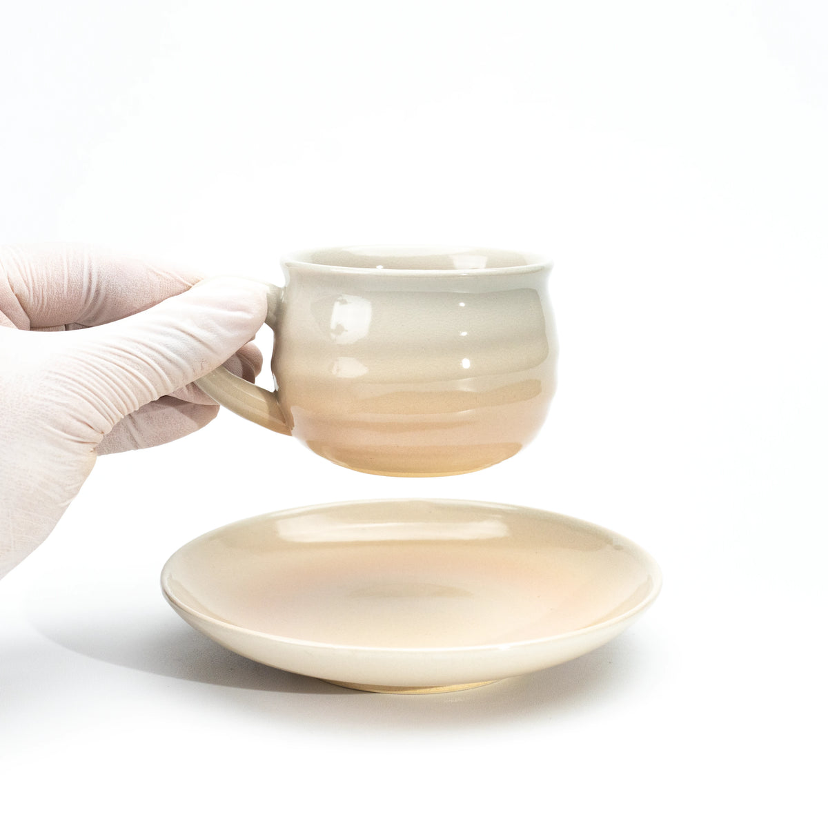 Hagi cup held above its matching saucer in a gloved hand.