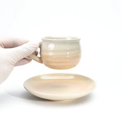 Hagi cup held above its matching saucer in a gloved hand.