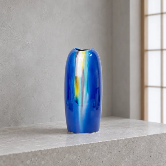 Hakuho Kutani Yusai blue porcelain vase displayed empty on a pale stone ledge in soft, cool daylight.