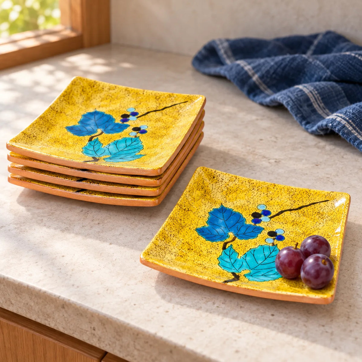 Four yellow Kutani wild grape square plates stacked beside a fifth plate holding a few fresh grapes
